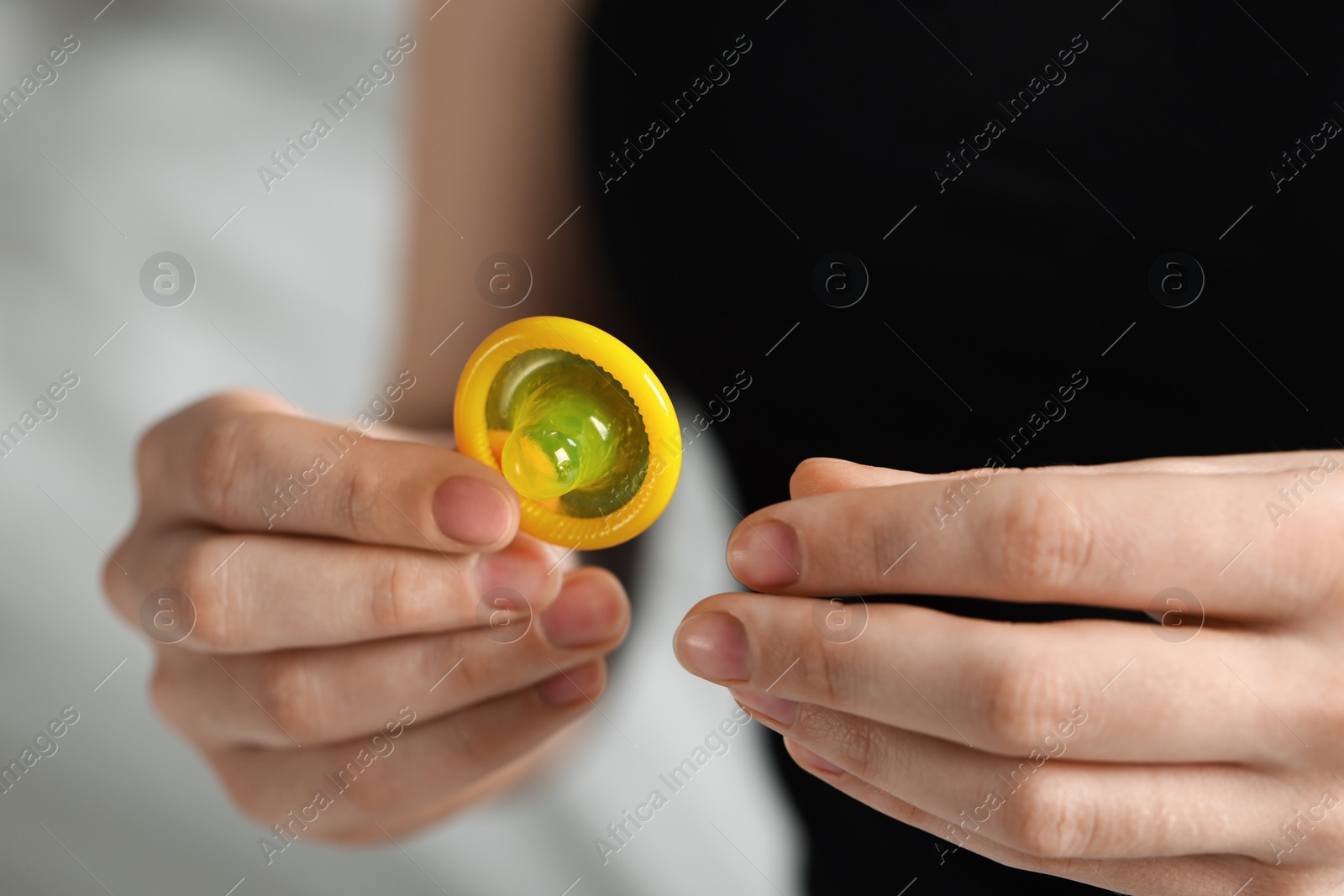 Photo of Woman holding unpacked condom on light background, closeup. Safe sex