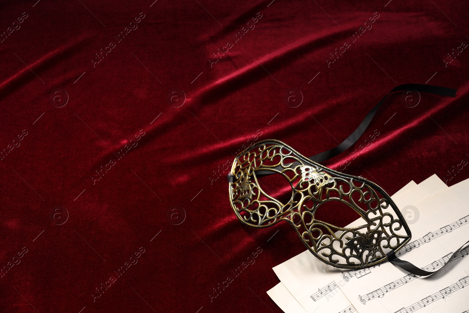 Photo of Elegant face mask and music sheets on red fabric, space for text. Theatrical performance