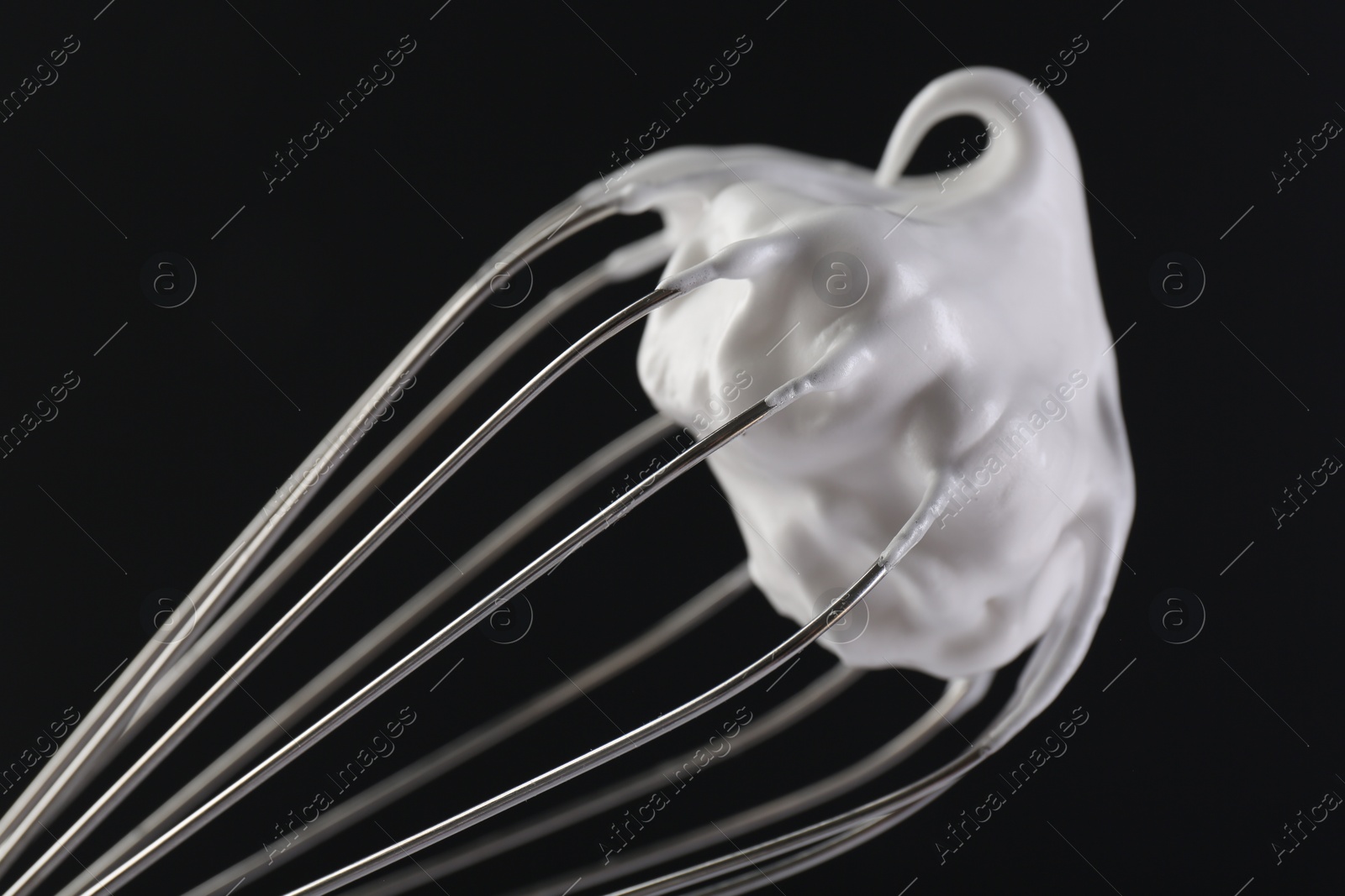 Photo of Whisk with whipped cream on black background, closeup