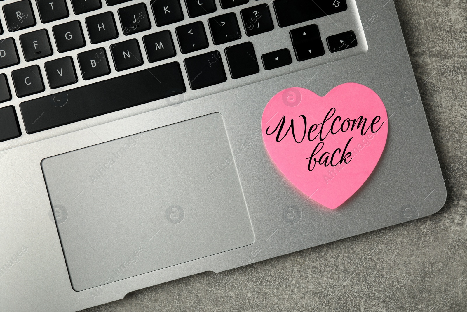 Image of Heart-shaped sticky note with phrase Welcome Back on laptop, top view