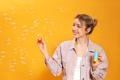 Photo of Young woman blowing soap bubbles on yellow background, space for text