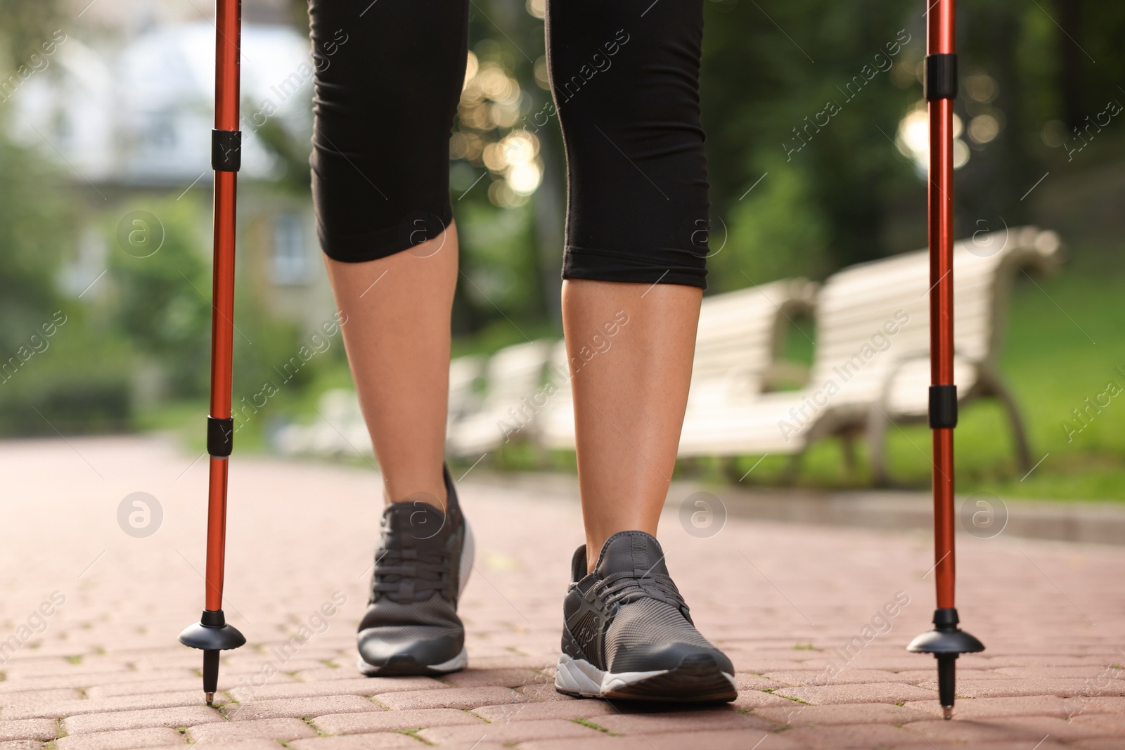 Photo of Young woman practicing Nordic walking with poles outdoors, closeup