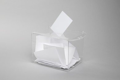Photo of Ballot box with votes on light grey background. Election time