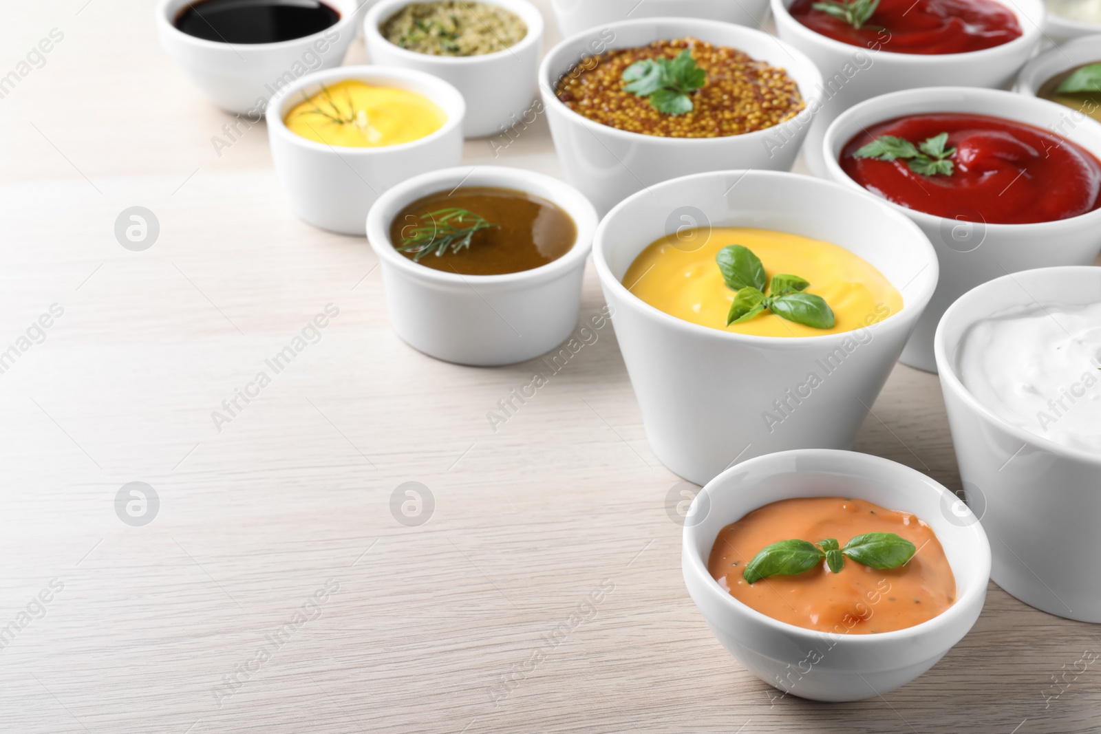 Photo of Many different sauces and herbs on wooden table. Space for text