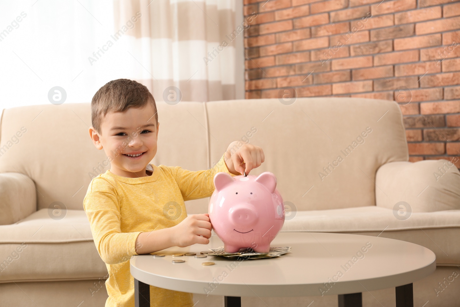 Photo of Little boy with piggy bank and money at home