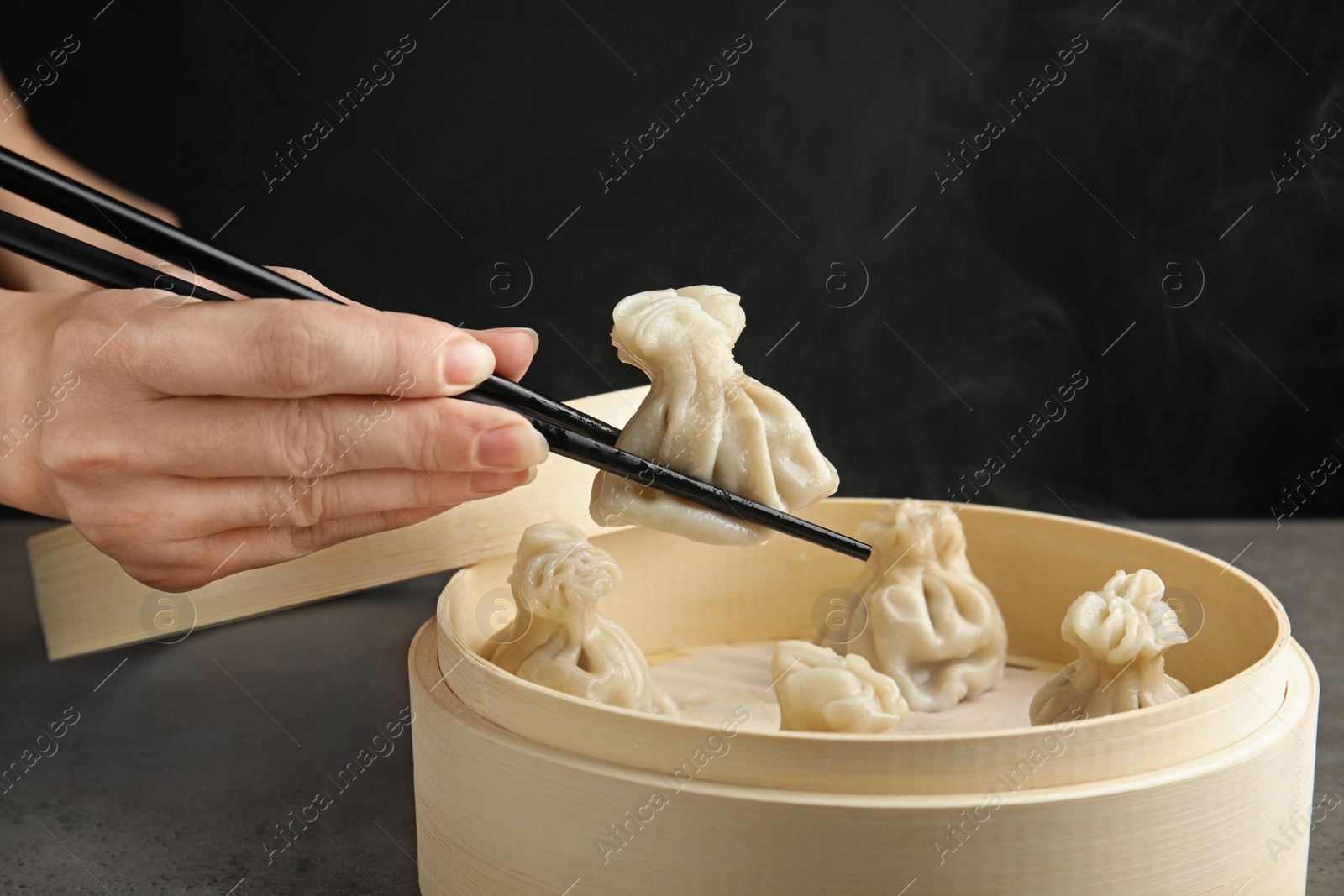 Photo of Woman cooking tasty baozi dumplings in bamboo steamer at table, closeup