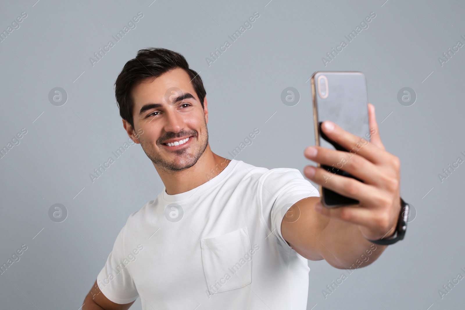 Photo of Handsome young man taking selfie with smartphone on grey background