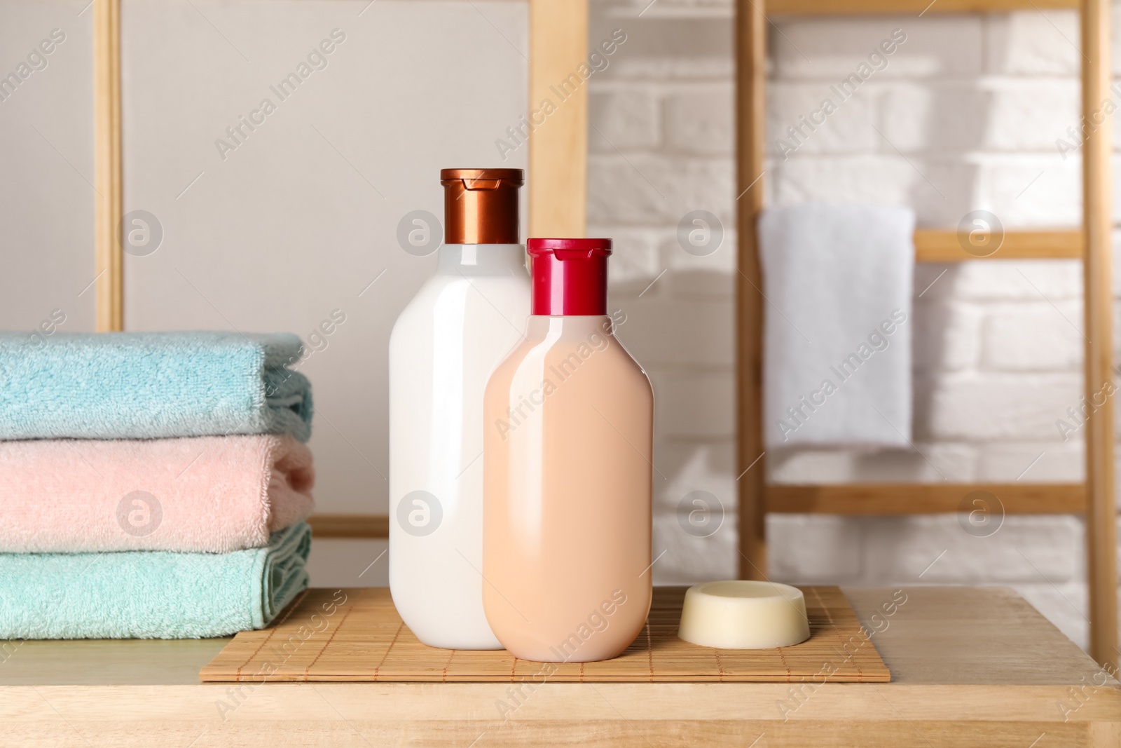 Photo of Solid shampoo bar and bottles of cosmetic product on wooden table in bathroom