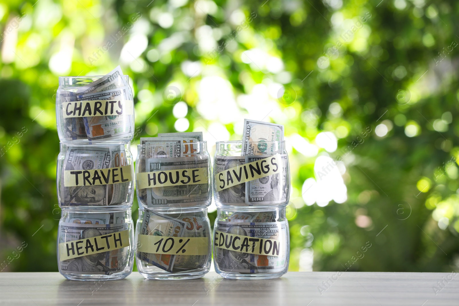 Photo of Glass jars with money for different needs on table against blurred background