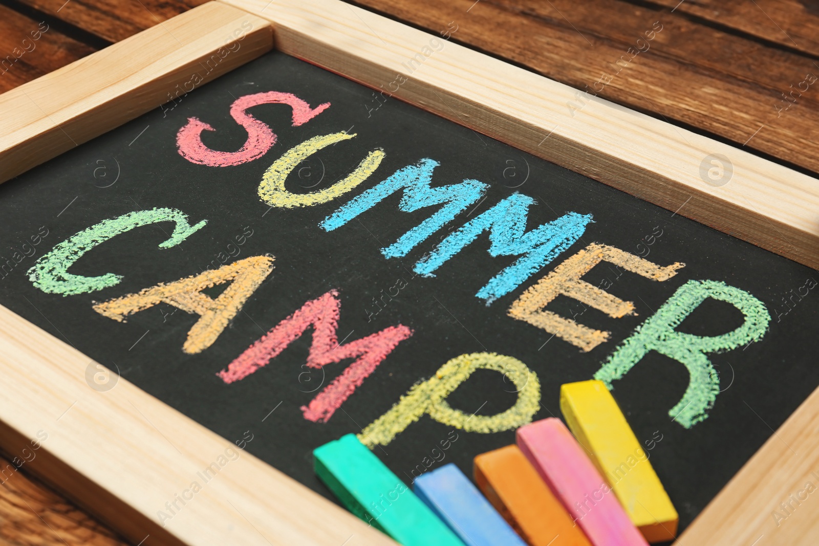 Photo of Little blackboard with text SUMMER CAMP chalked in different colors on table