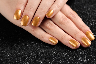 Photo of Woman showing manicured hands with golden nail polish on black background, closeup