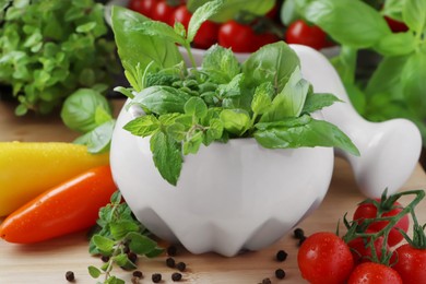 Photo of Mortar with different fresh herbs and pepper on wooden table, closeup
