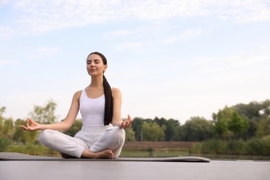 Beautiful young woman practicing Padmasana on yoga mat outdoors, low angle view. Lotus pose