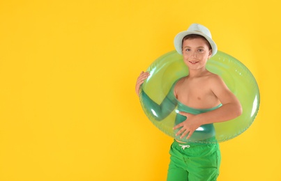 Cute little child in beachwear with bright inflatable ring on yellow background. Space for text