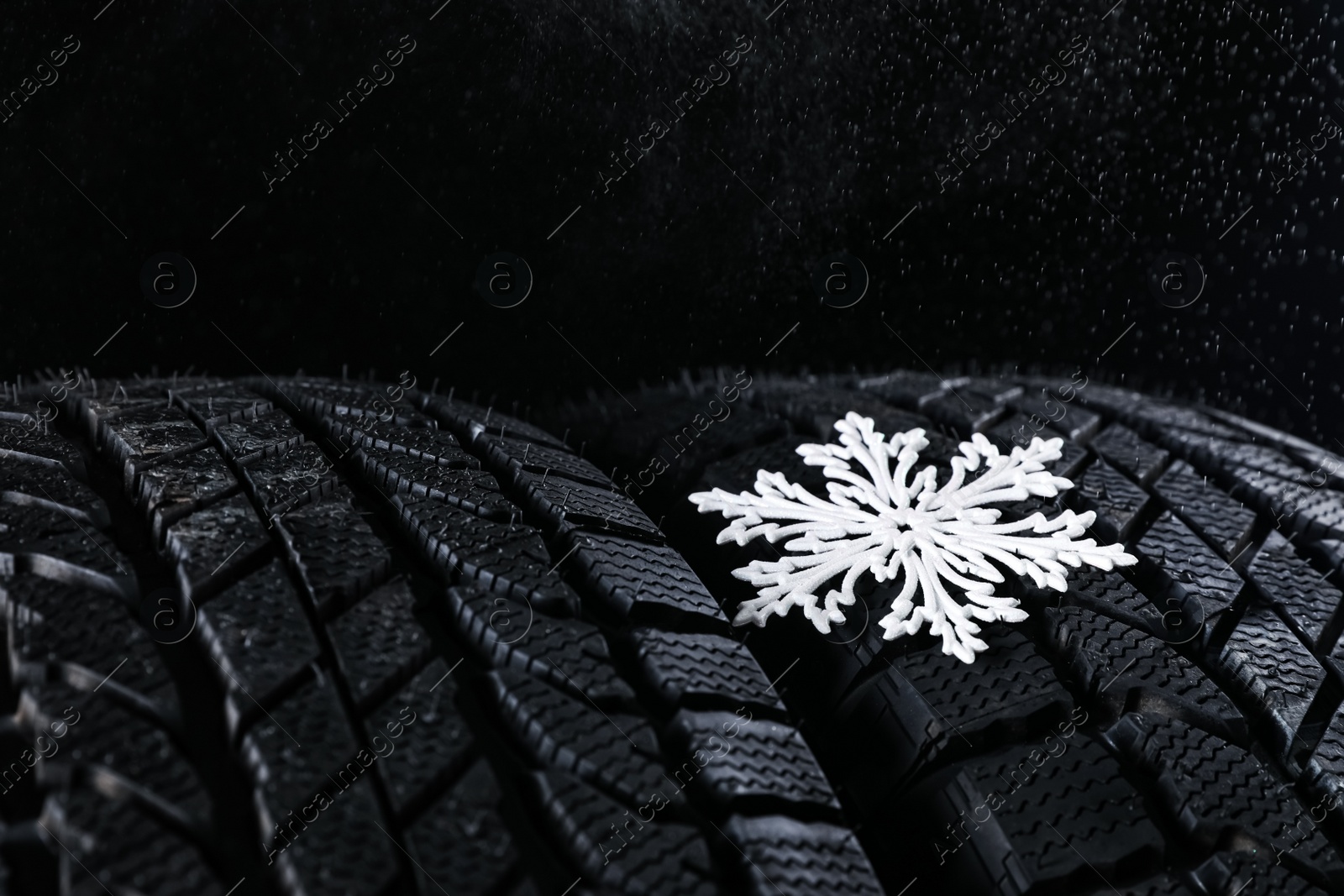 Photo of Winter tires with decorative snowflake on black background, closeup