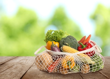 Fresh vegetables in mesh bag on wooden table against blurred background