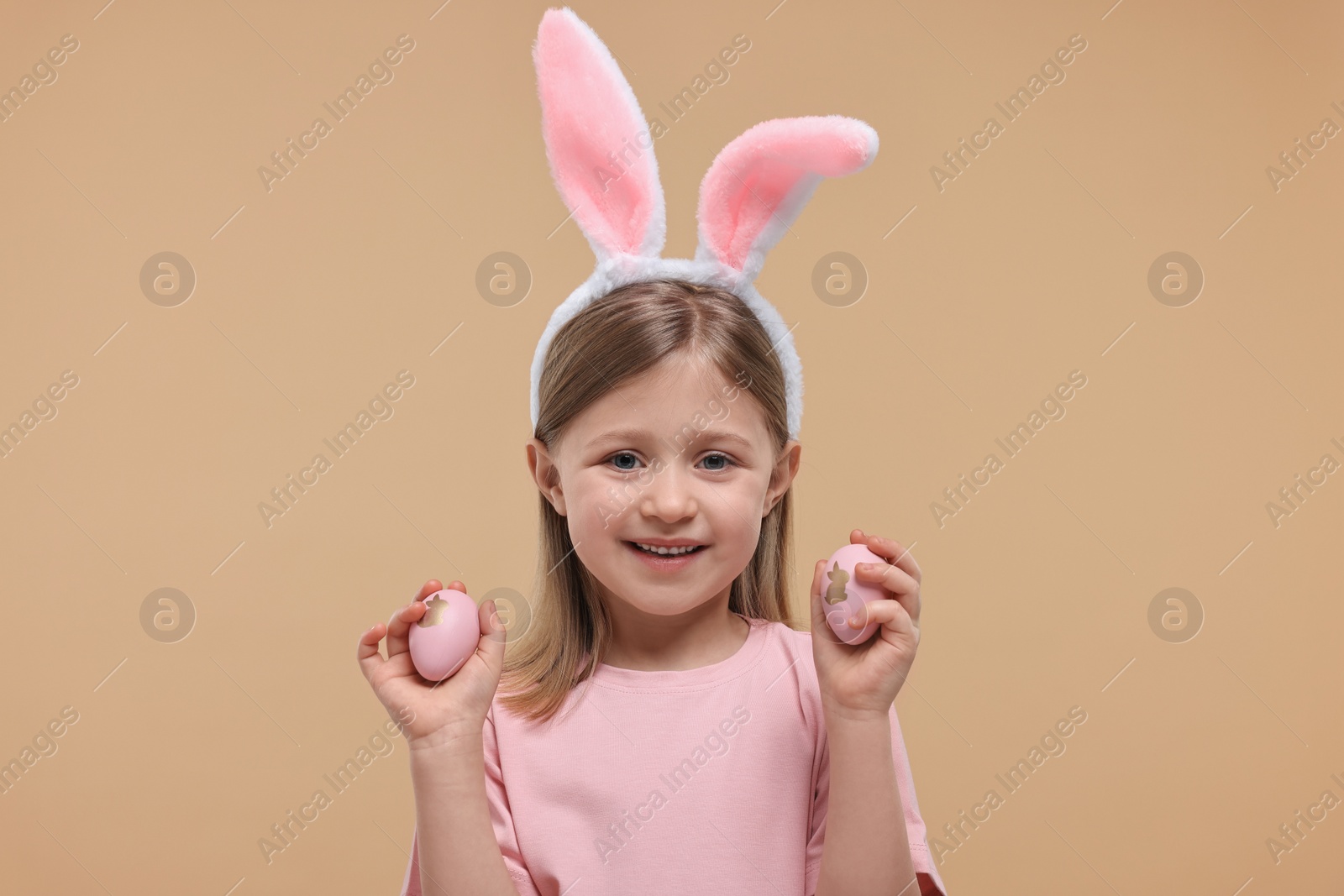 Photo of Easter celebration. Cute girl with bunny ears holding eggs on beige background