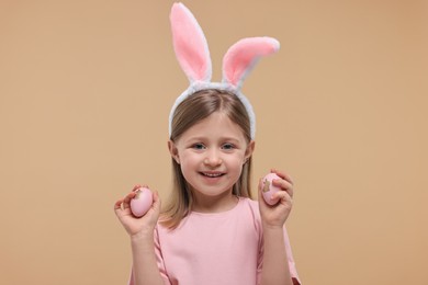 Easter celebration. Cute girl with bunny ears holding eggs on beige background