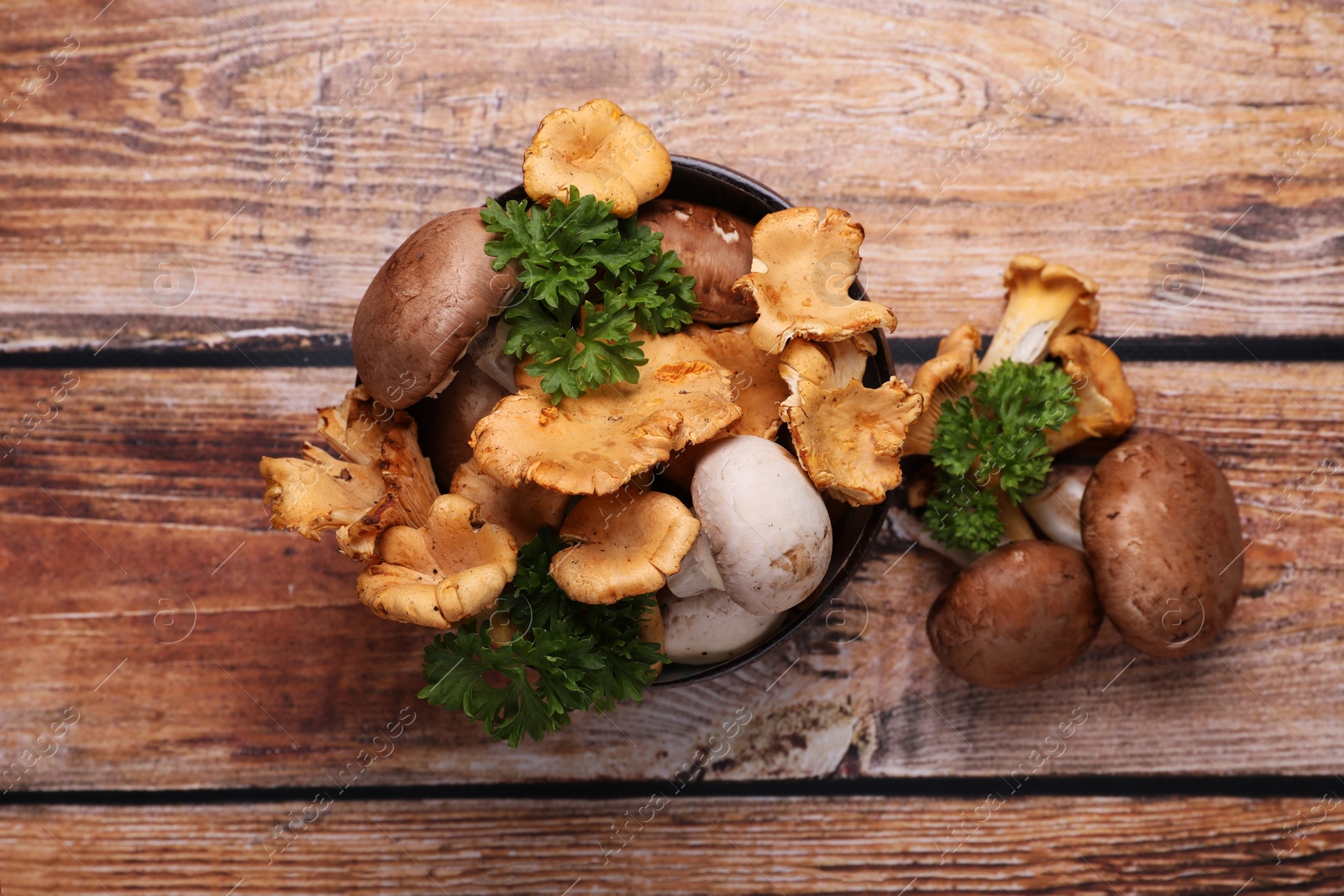 Photo of Bowl with different mushrooms and parsley on wooden table, flat lay