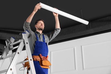 Electrician in uniform installing ceiling lamp indoors