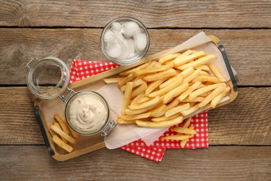 Photo of Delicious french fries served with sauce and glass of water on wooden table, flat lay