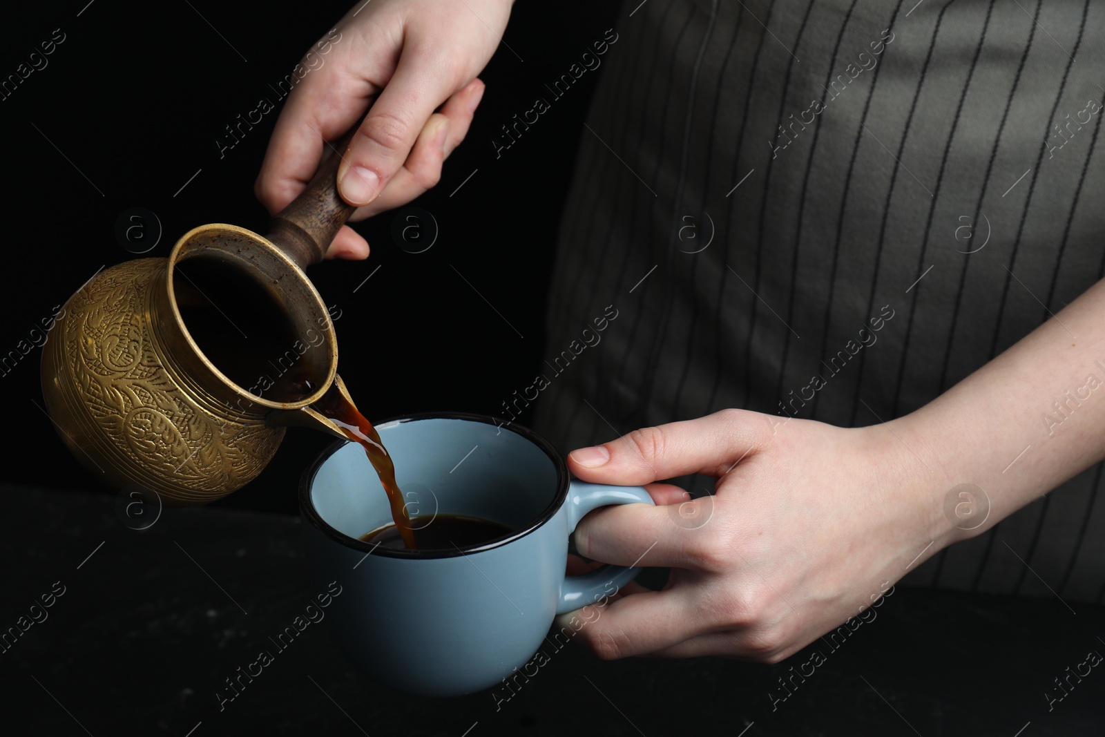 Photo of Turkish coffee. Woman pouring brewed beverage from cezve into cup at black table, closeup