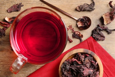 Photo of Cup of fresh hibiscus tea and dry flower leaves on wooden table, flat lay