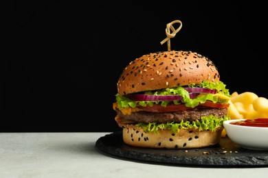 Photo of Burger with delicious patty, french fries and sauce on gray table against black background, space for text