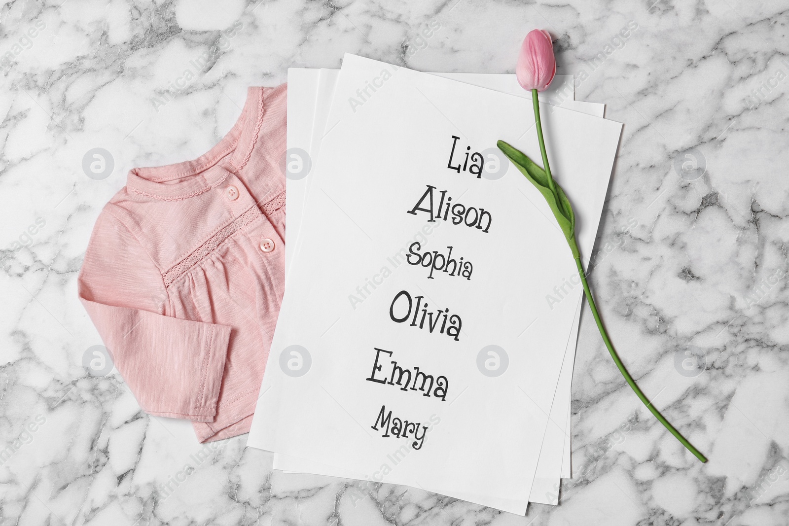 Photo of List of baby names, tulip flower and child's clothes on white marble background, flat lay