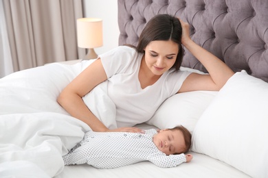 Happy woman with her sleeping baby on bed