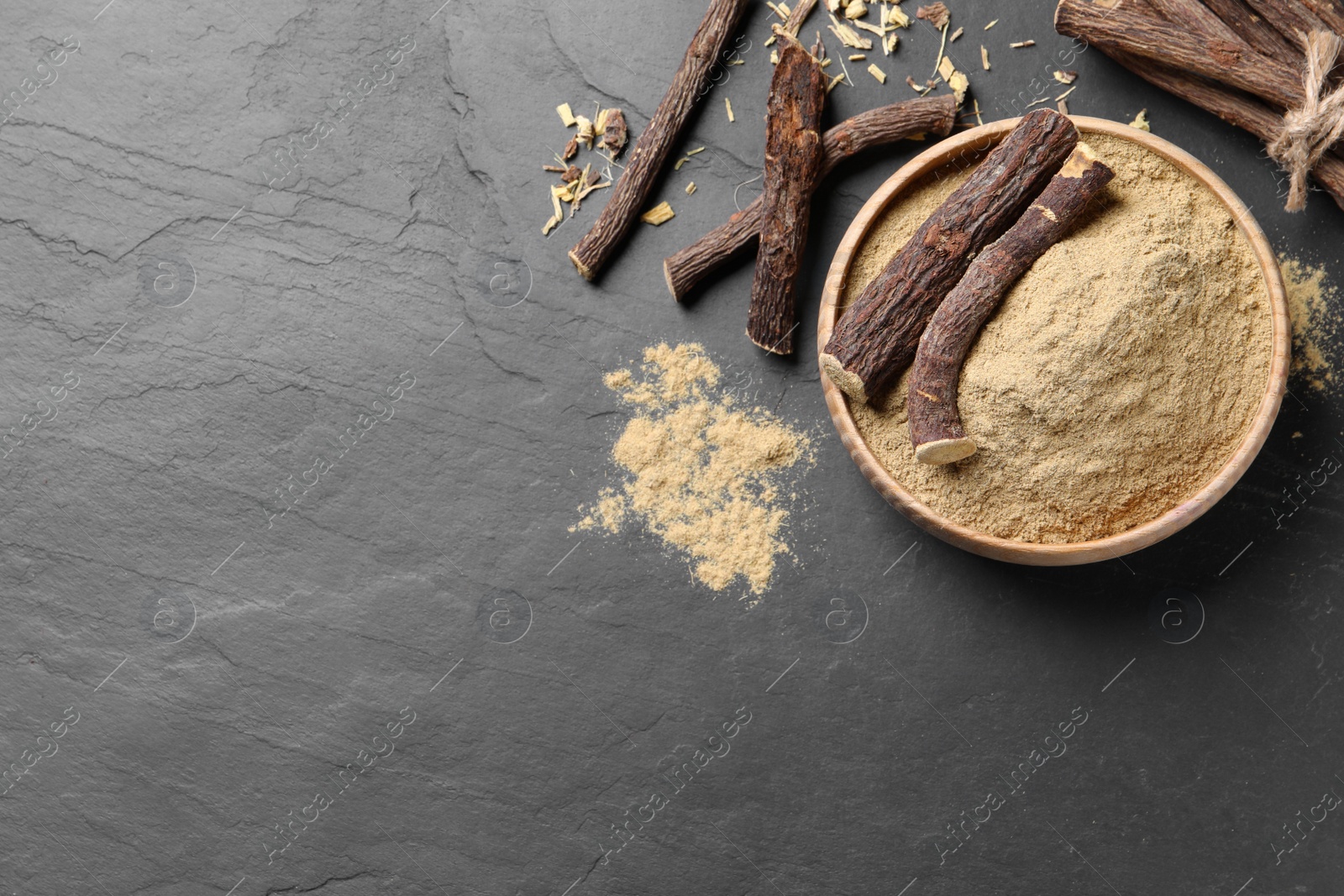 Photo of Powder in bowl and dried sticks of liquorice root on black table, flat lay. Space for text