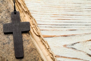 Photo of Wooden Christian cross and old Bible on white table, top view. Space for text