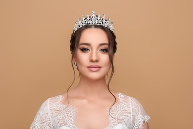 Beautiful young woman wearing luxurious tiara on beige background