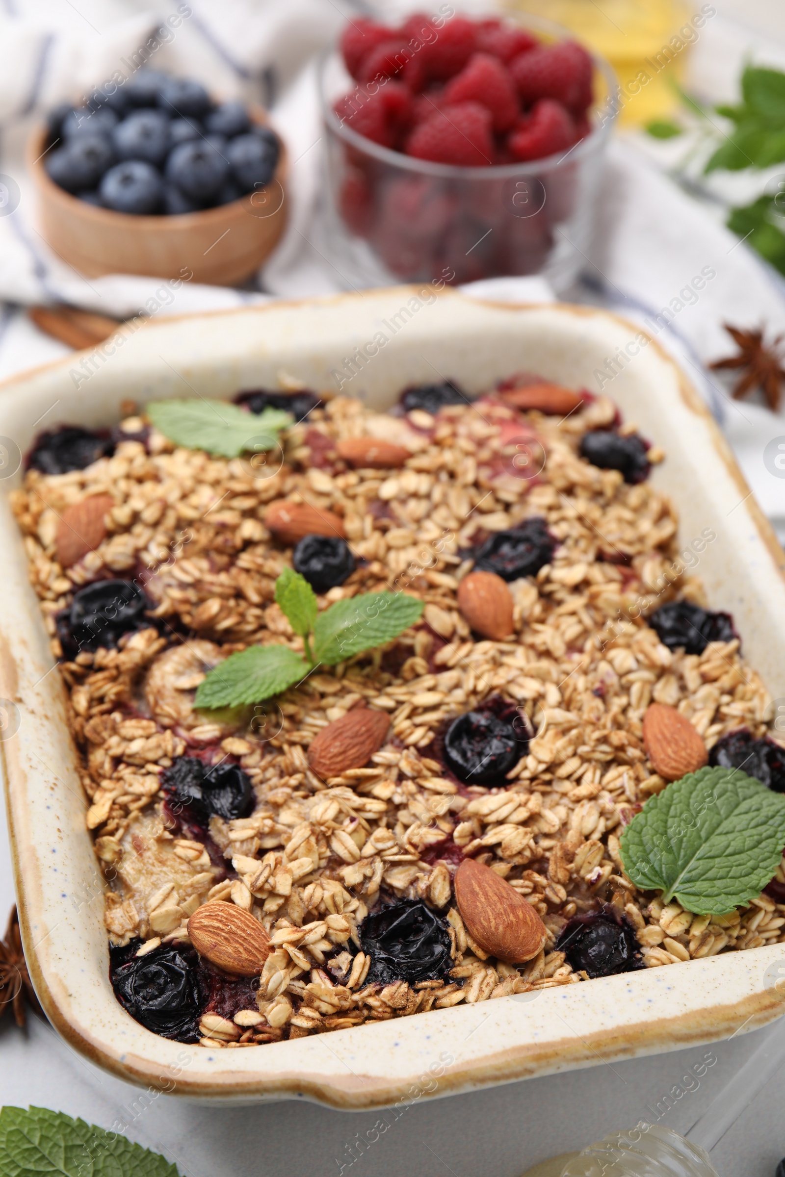 Photo of Tasty baked oatmeal with berries and almonds in baking tray on white table, closeup