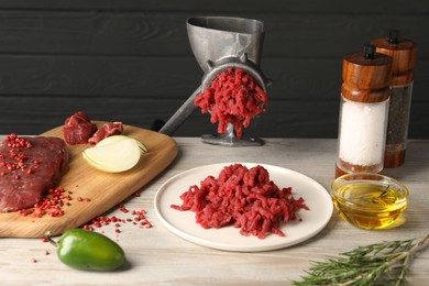 Metal meat grinder with minced beef and products on light wooden table