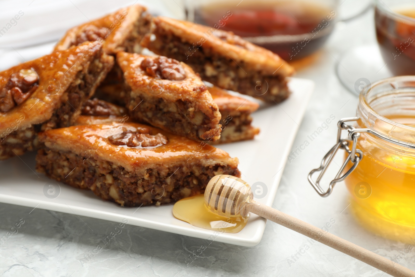 Photo of Delicious baklava with walnuts and honey on light grey marble table, closeup