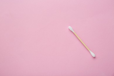 One wooden cotton bud on pink background, top view. Space for text