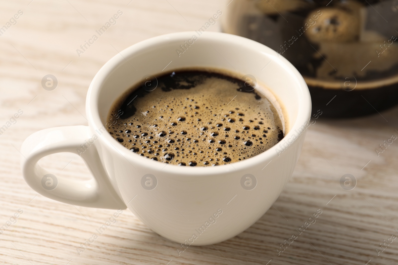 Photo of Aromatic coffee in cup on light wooden table, closeup