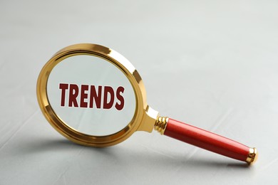 Image of Searching new and popular trends. Magnifying glass with word on light grey table, closeup