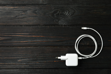 White charging cable and adapter on black wooden table, top view. Space for text