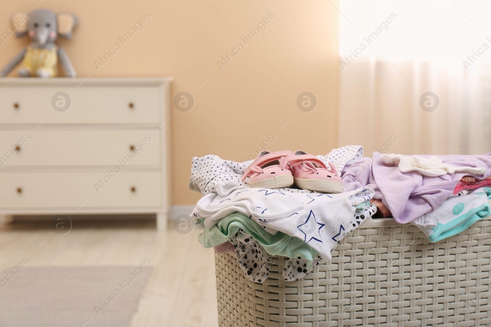 Photo of Laundry basket with baby clothes in child room, closeup. Space for text