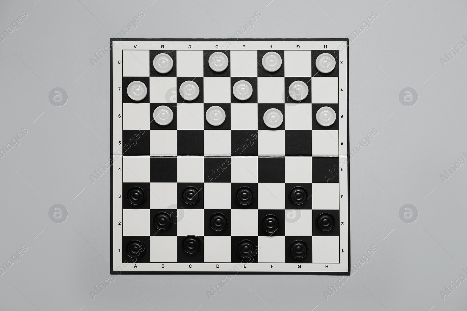 Photo of Black and white checkerboard with game pieces on light grey background, top view