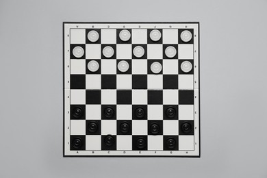 Photo of Black and white checkerboard with game pieces on light grey background, top view