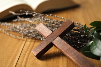 Photo of Cross and willow branches on wooden table, closeup