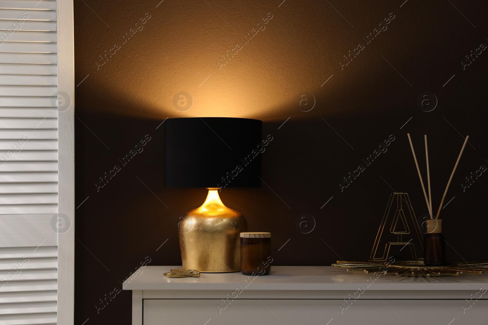 Photo of Stylish lamp and decor on white table near brown wall indoors. Interior design