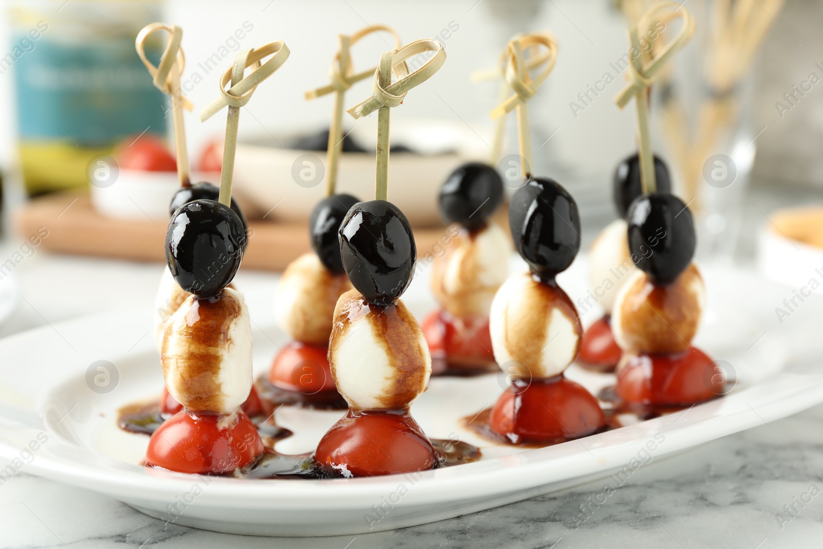 Photo of Tasty canapes with black olives, mozzarella and cherry tomatoes on white marble table, closeup