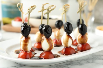 Tasty canapes with black olives, mozzarella and cherry tomatoes on white marble table, closeup