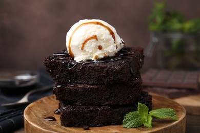 Photo of Delicious brownies served with ice cream and caramel sauce on table, closeup