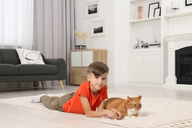 Little boy and cute ginger cat on soft carpet at home