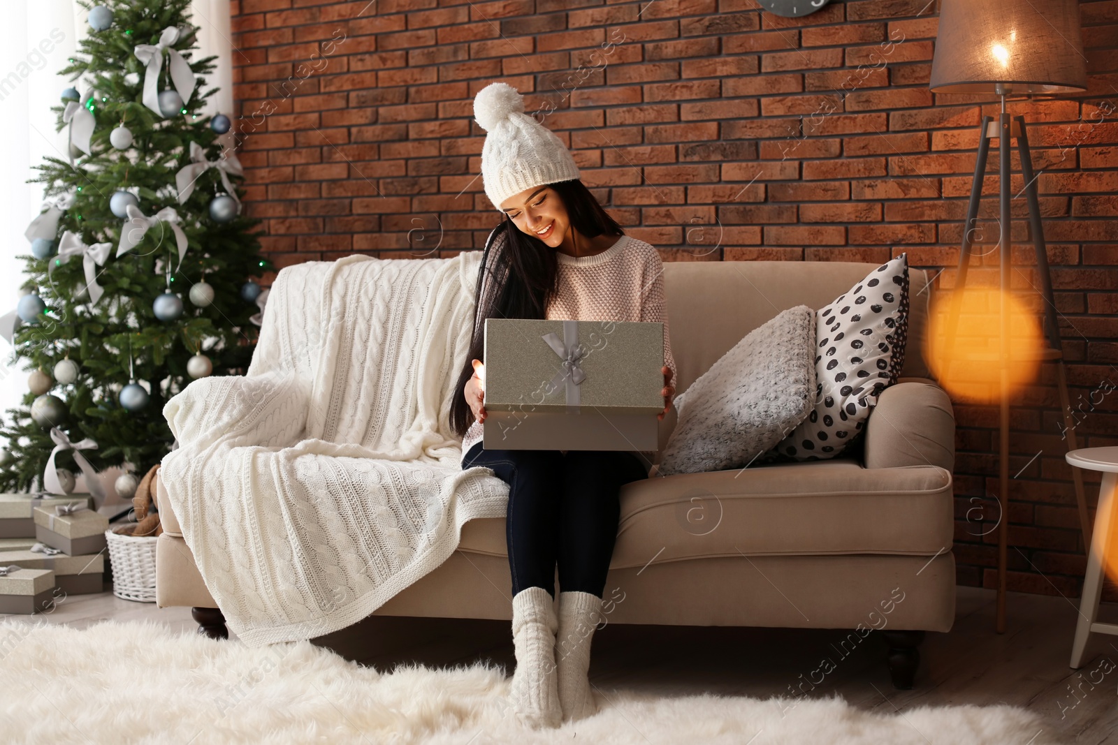 Photo of Beautiful young woman in hat opening gift box at home. Christmas celebration